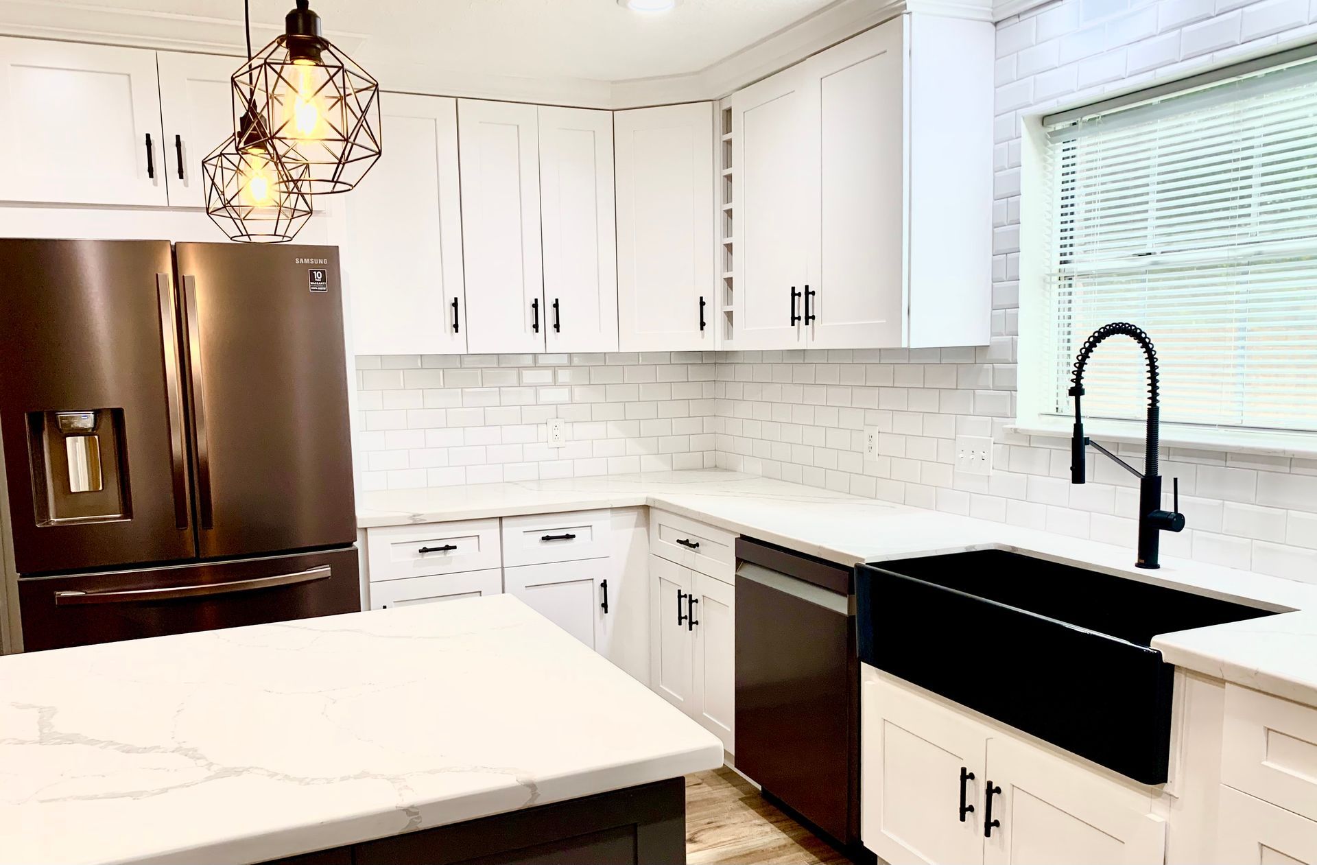 Modern white kitchen with stainless steel appliances, black sink, and pendant lights.