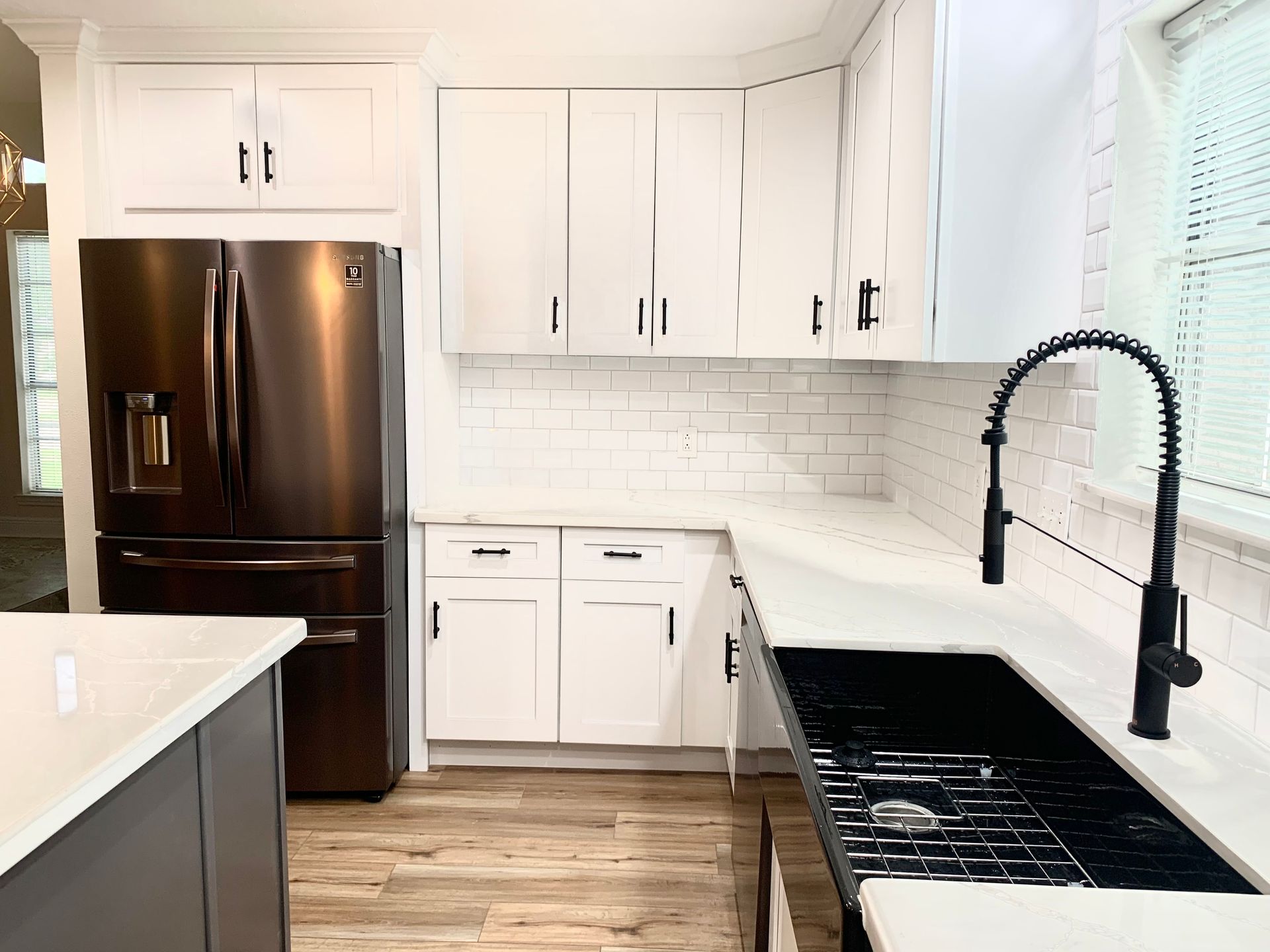 Modern white kitchen with stainless steel refrigerator, white cabinets, black sink and faucet.