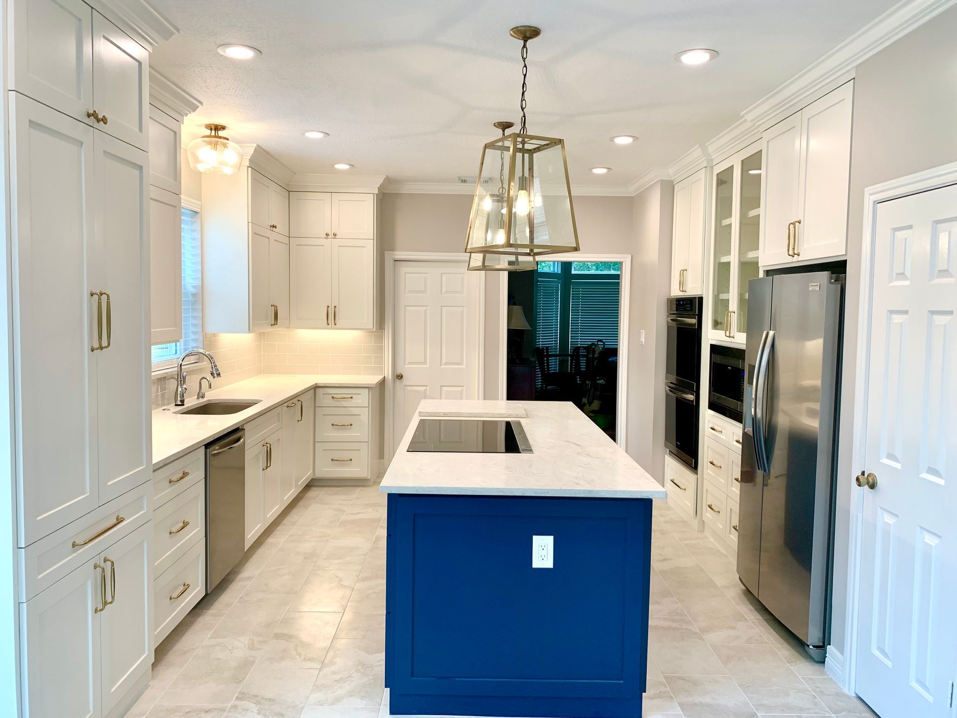 Modern kitchen with white cabinets, blue island, stainless steel appliances, and gold hardware.