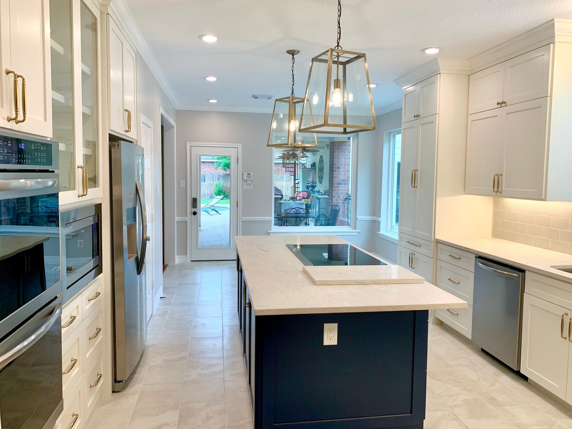 Modern white kitchen with blue island, stainless steel appliances, and outdoor view.