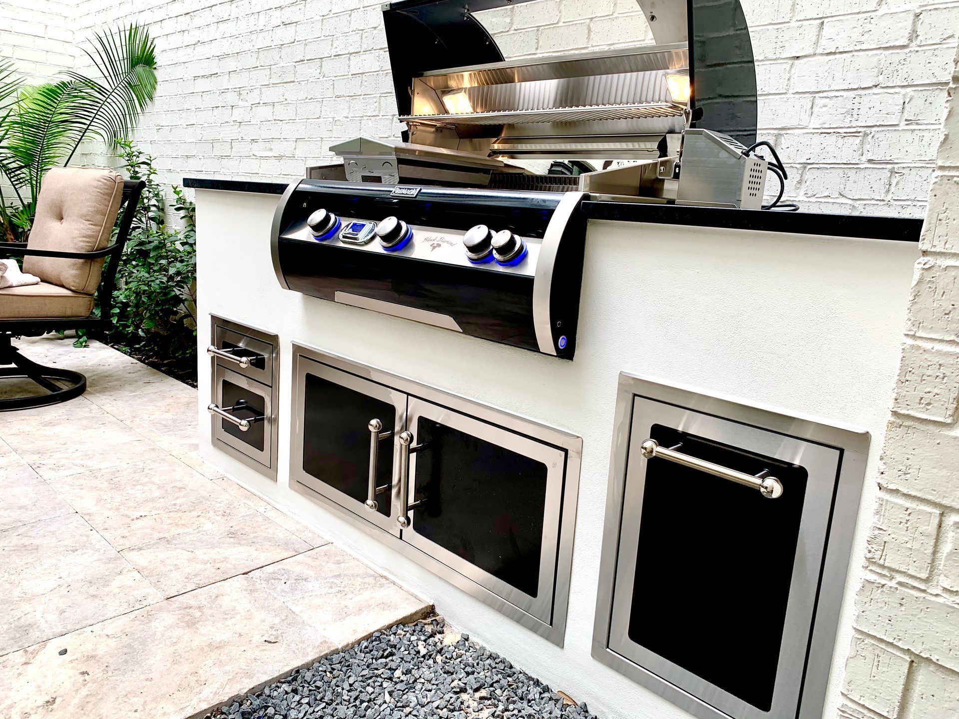 Outdoor kitchen island with stainless steel grill, oven, and storage cabinets, set on stone patio.