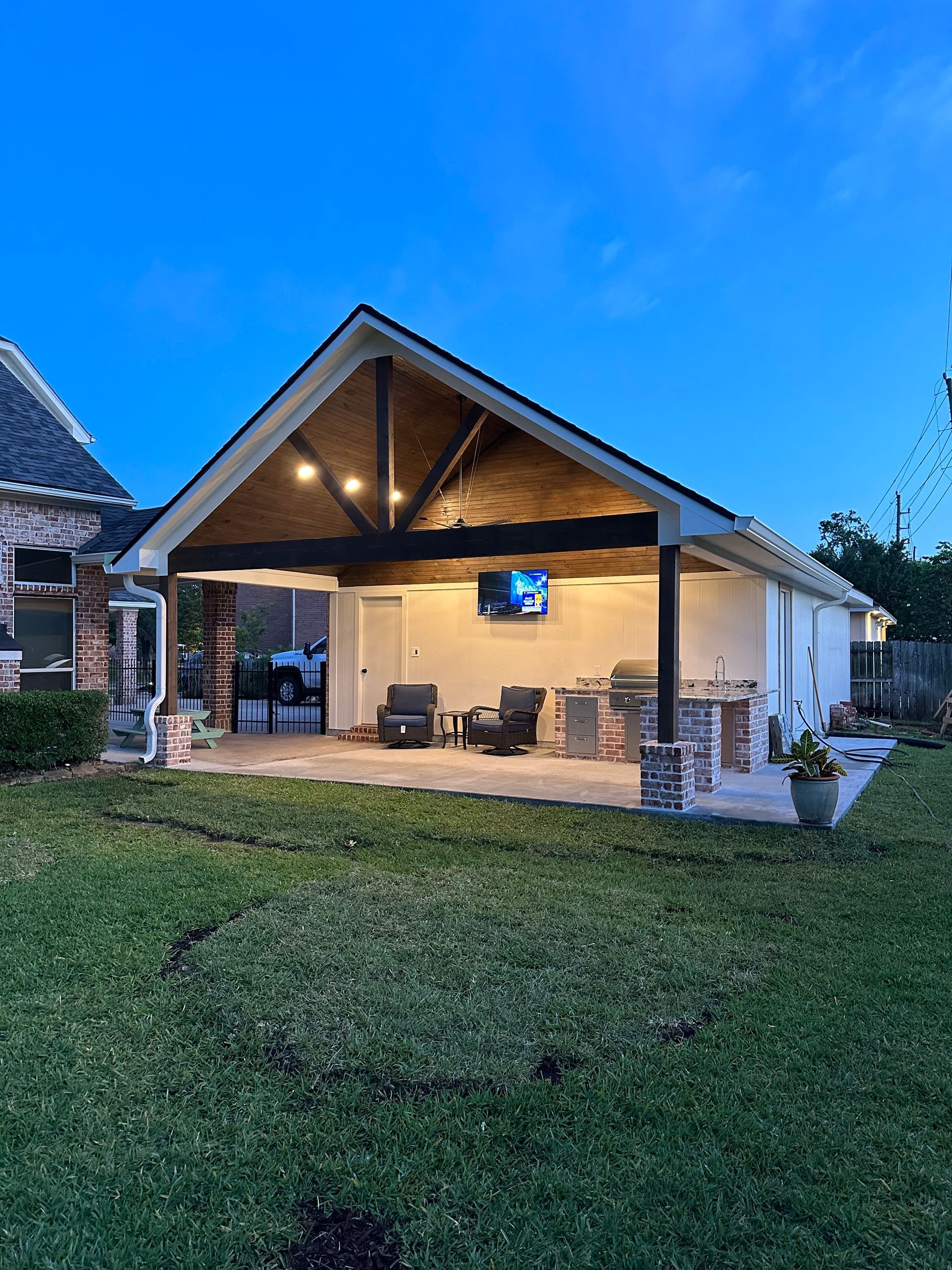 Backyard patio with an open-air roof and TV. Features outdoor seating, a grill, and a brick accent.