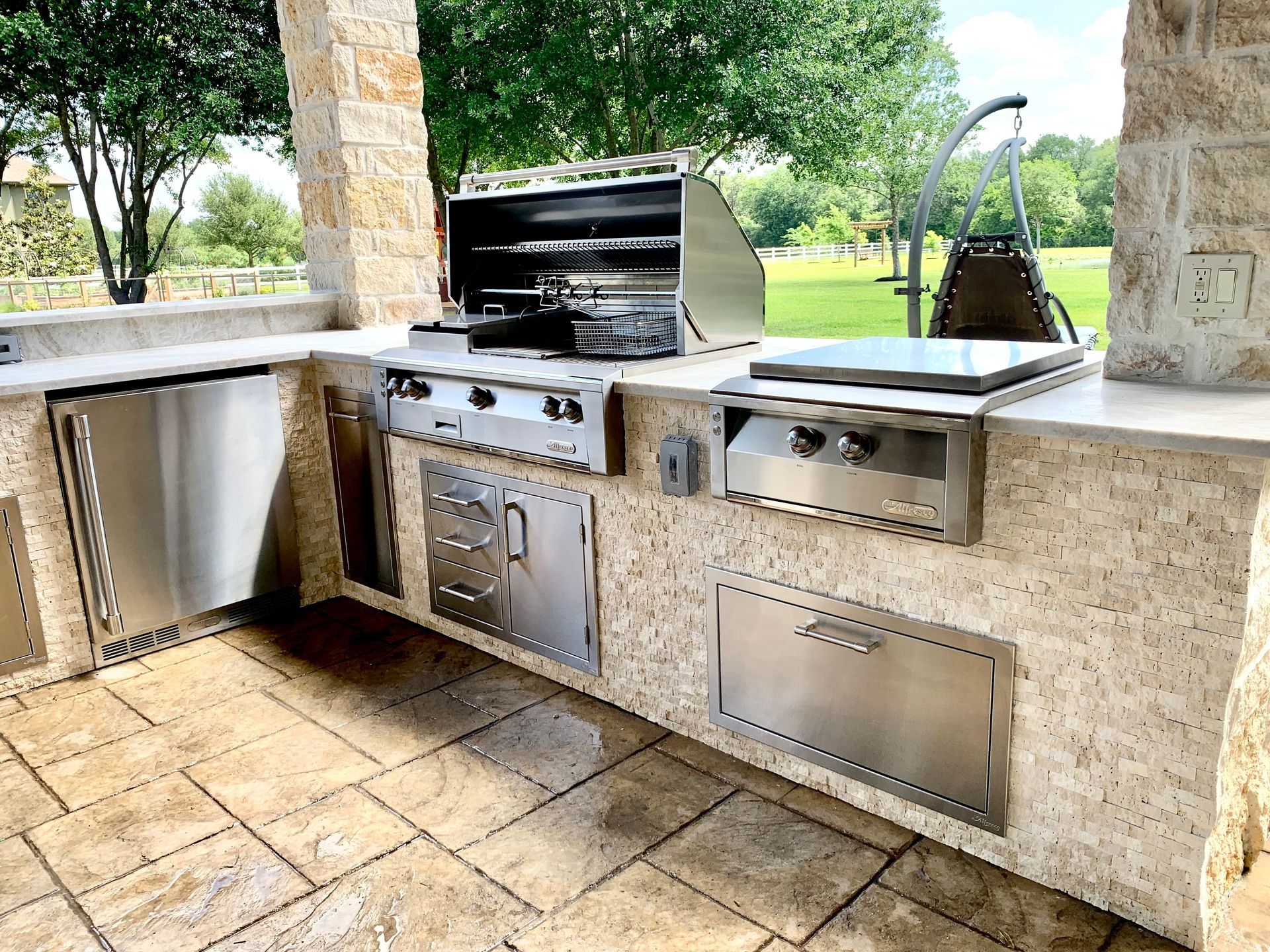 Outdoor kitchen with stainless steel appliances set in a stone countertop and base.