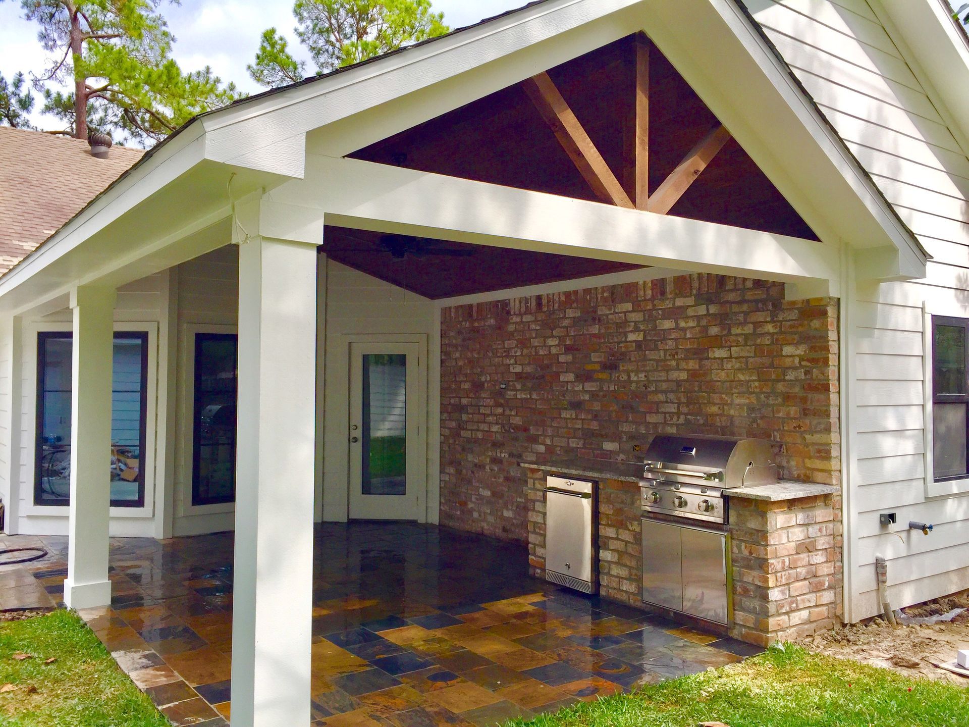 Outdoor kitchen area with brick, stainless steel grill, and white columns under a gable roof.