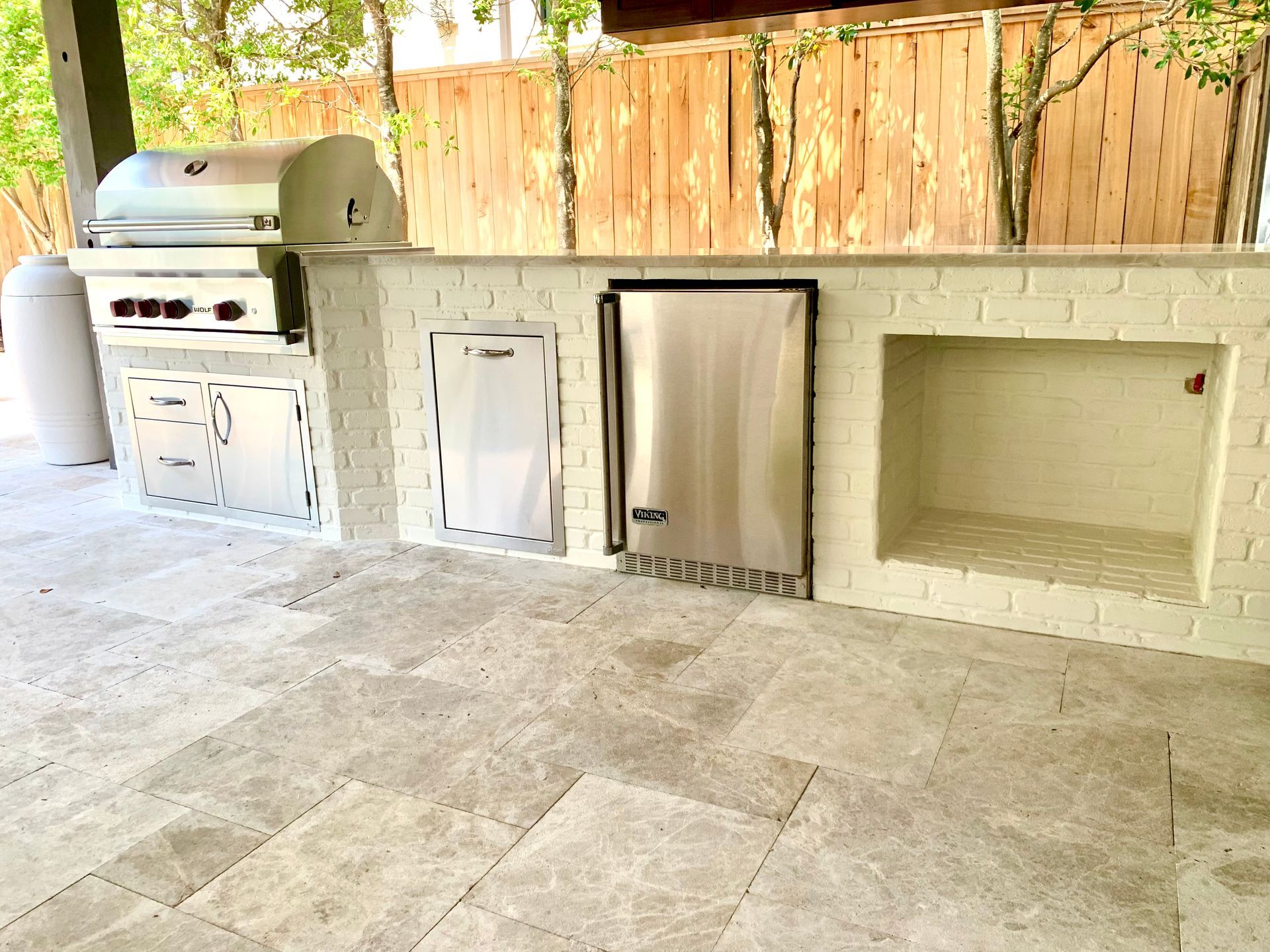 Outdoor kitchen with grill, refrigerator, and storage on a stone patio. 