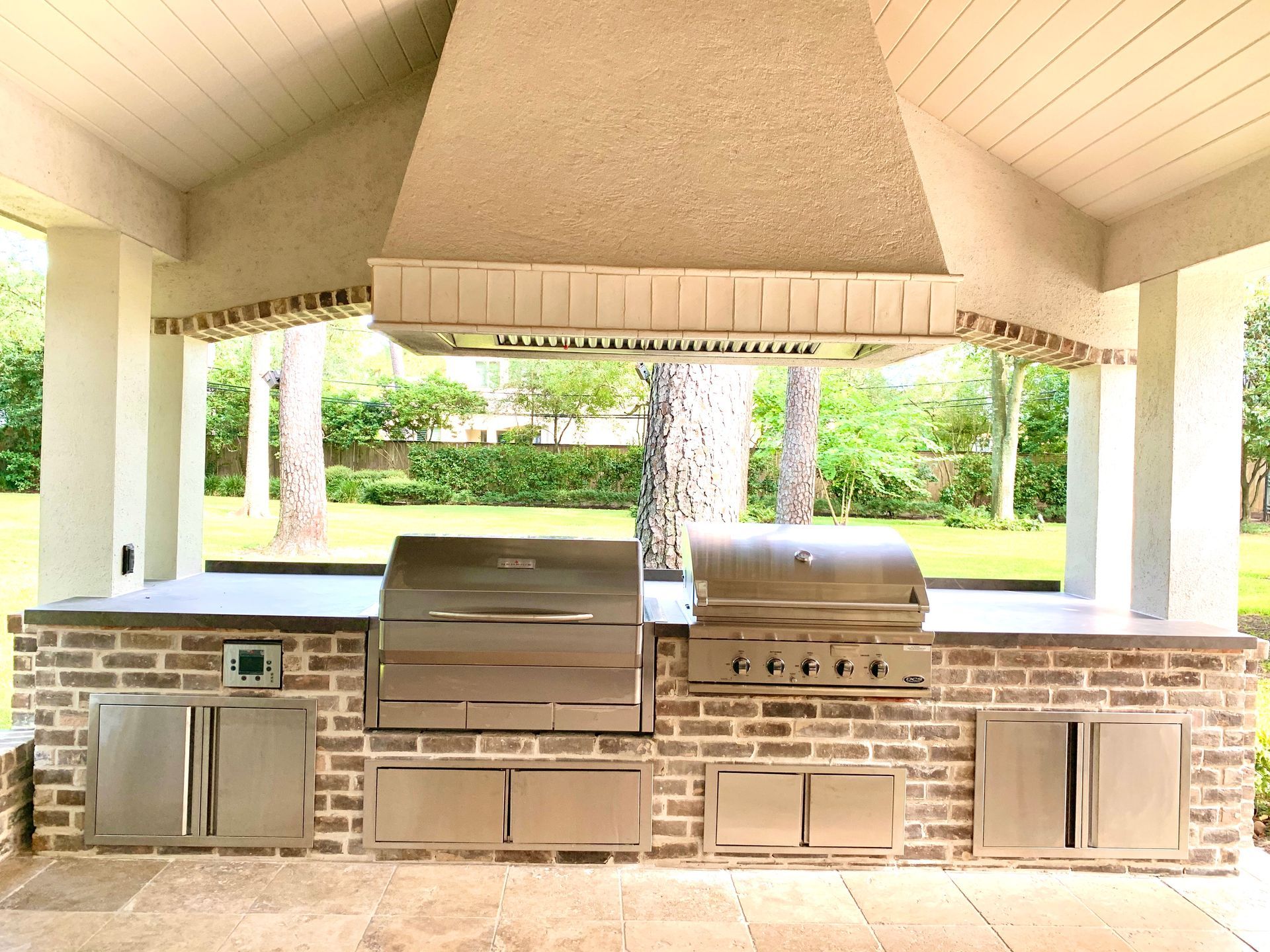 Outdoor kitchen with stainless steel grills, brick facade, and tan stucco range hood.