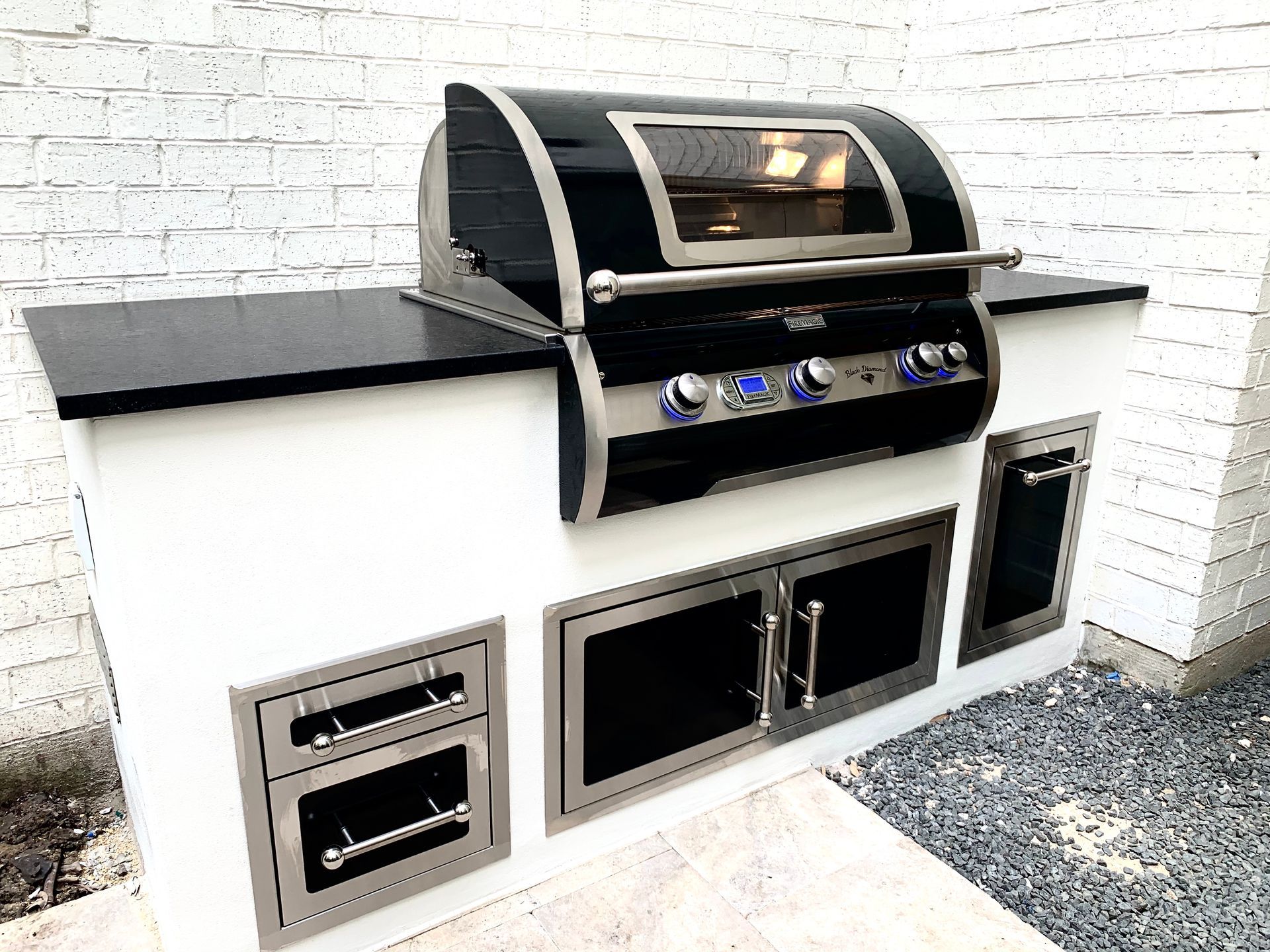 Outdoor kitchen with a black and stainless steel grill, white cabinetry, and a black countertop.