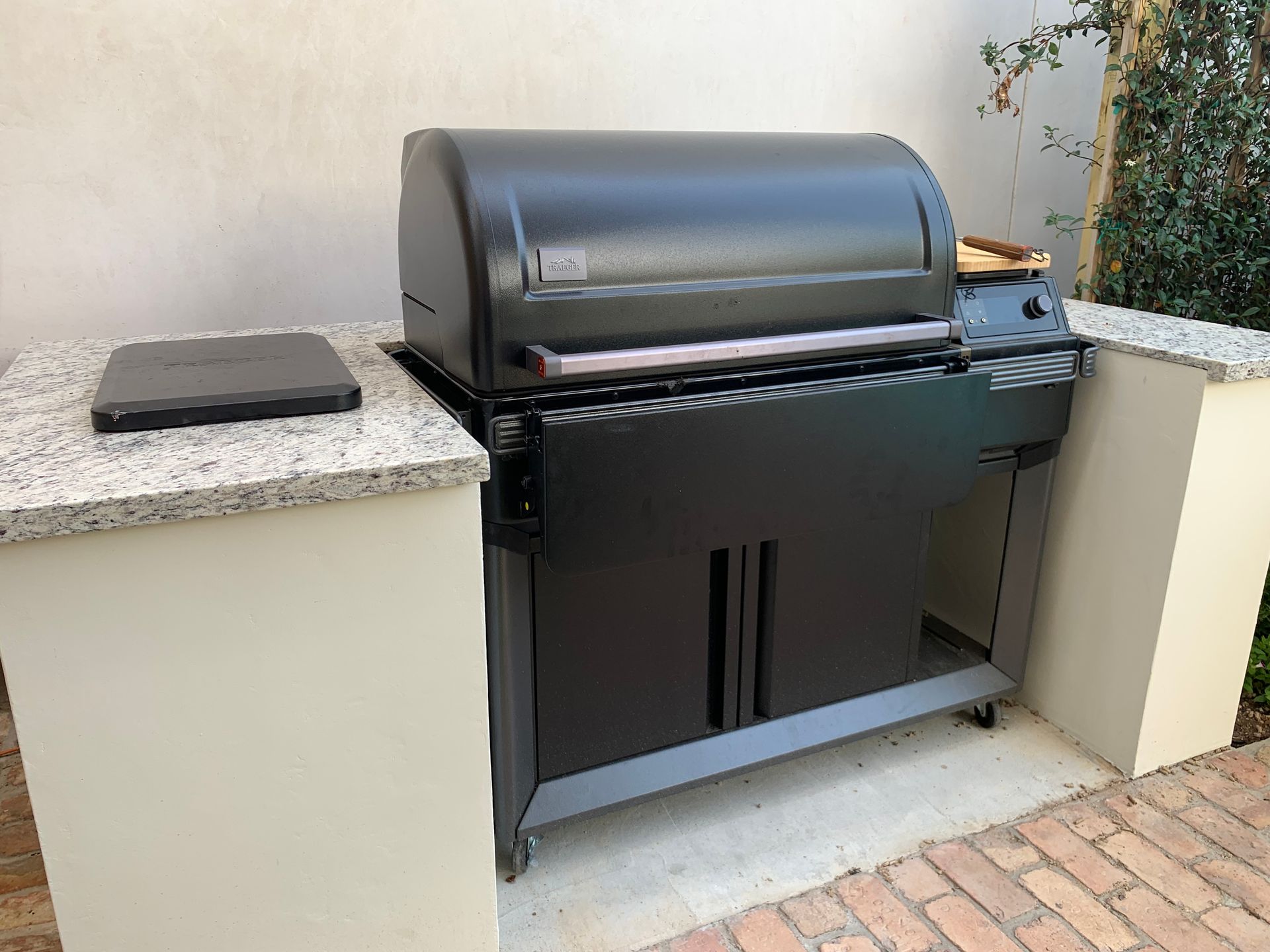 Black grill on a granite countertop, built into a stucco structure, next to a brick patio.