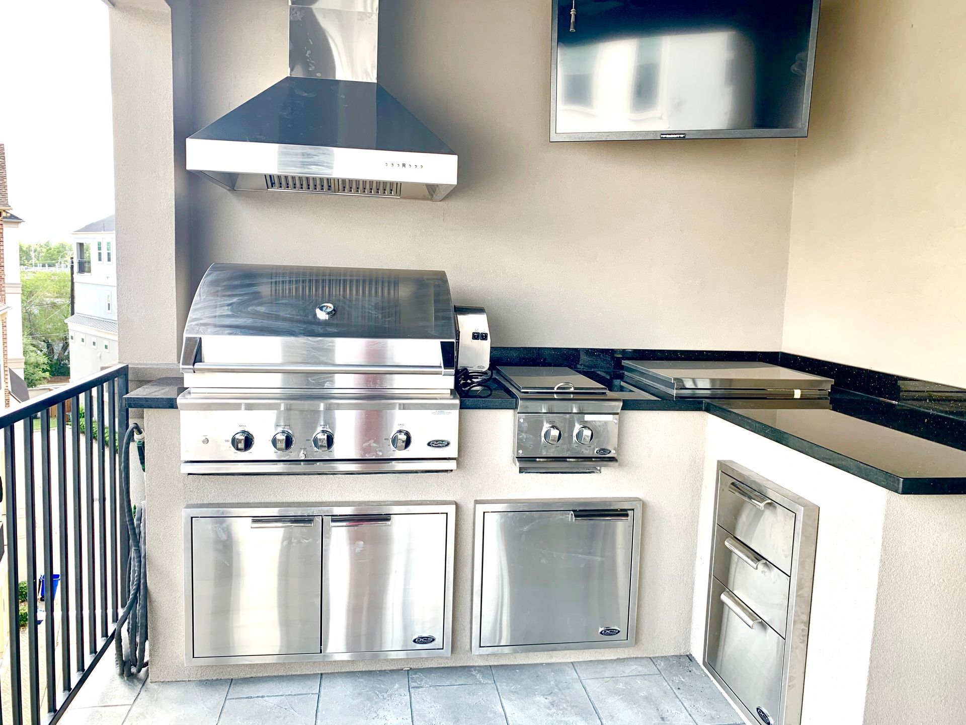 Outdoor kitchen with stainless steel grill, hood, storage, and a built-in TV.