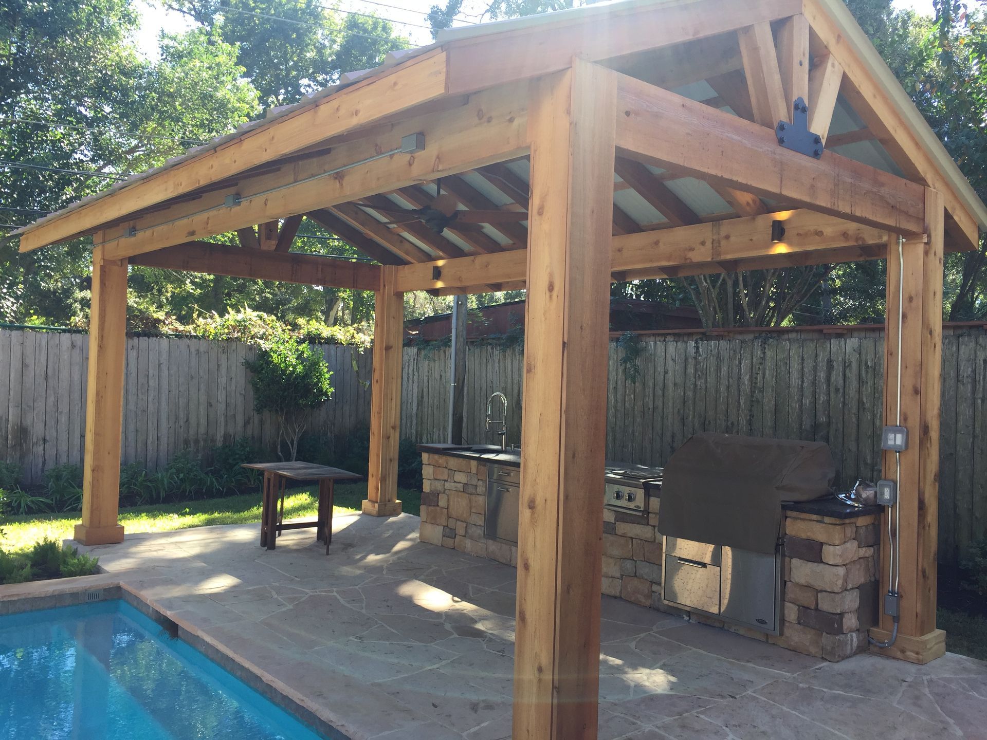 Wooden outdoor kitchen and patio cover over a grill and pool.