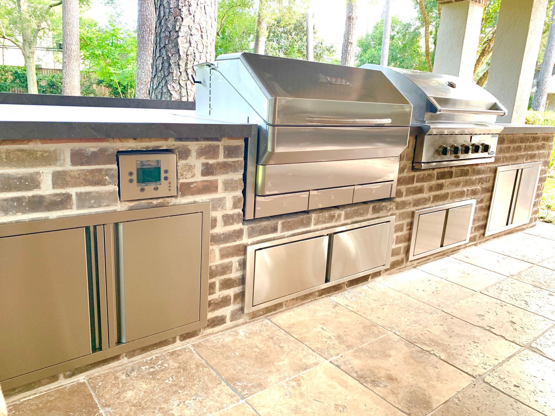 Outdoor kitchen with stainless steel grill, brick facade, and stone patio.