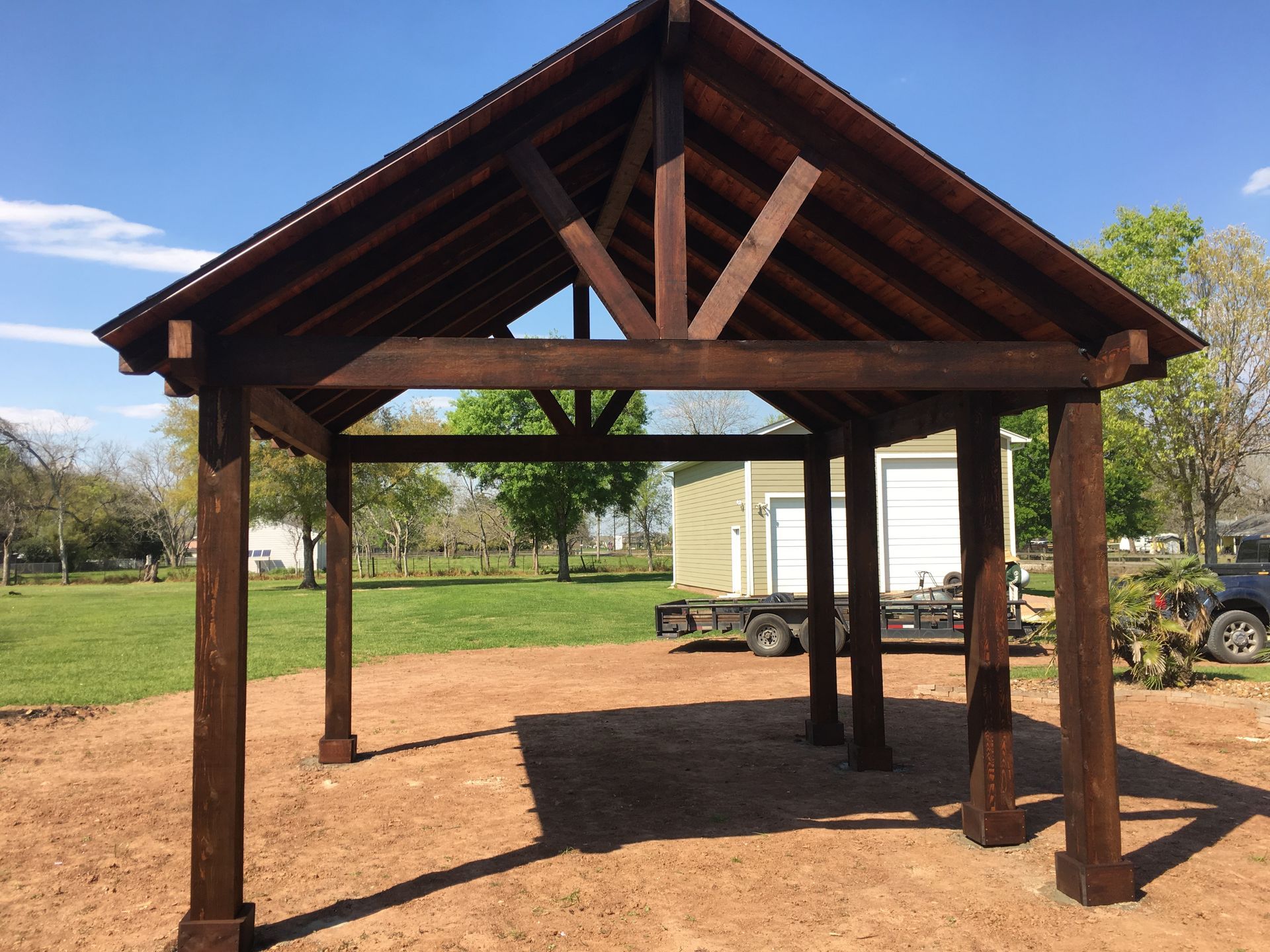 Wooden pavilion with dark brown stain on a sunny day in a grassy field.