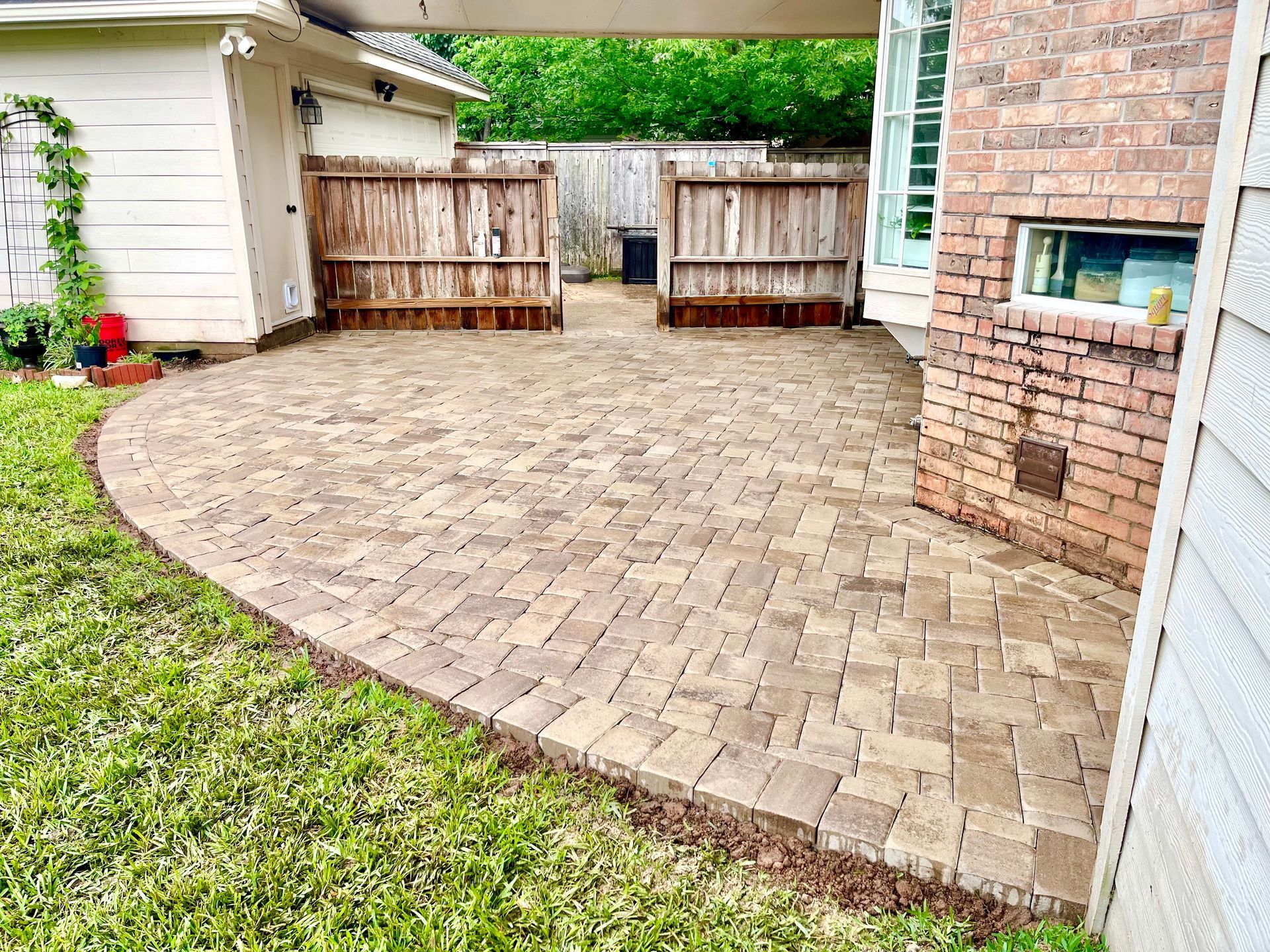Brick patio next to a building and lawn, leading to a wooden fence.
