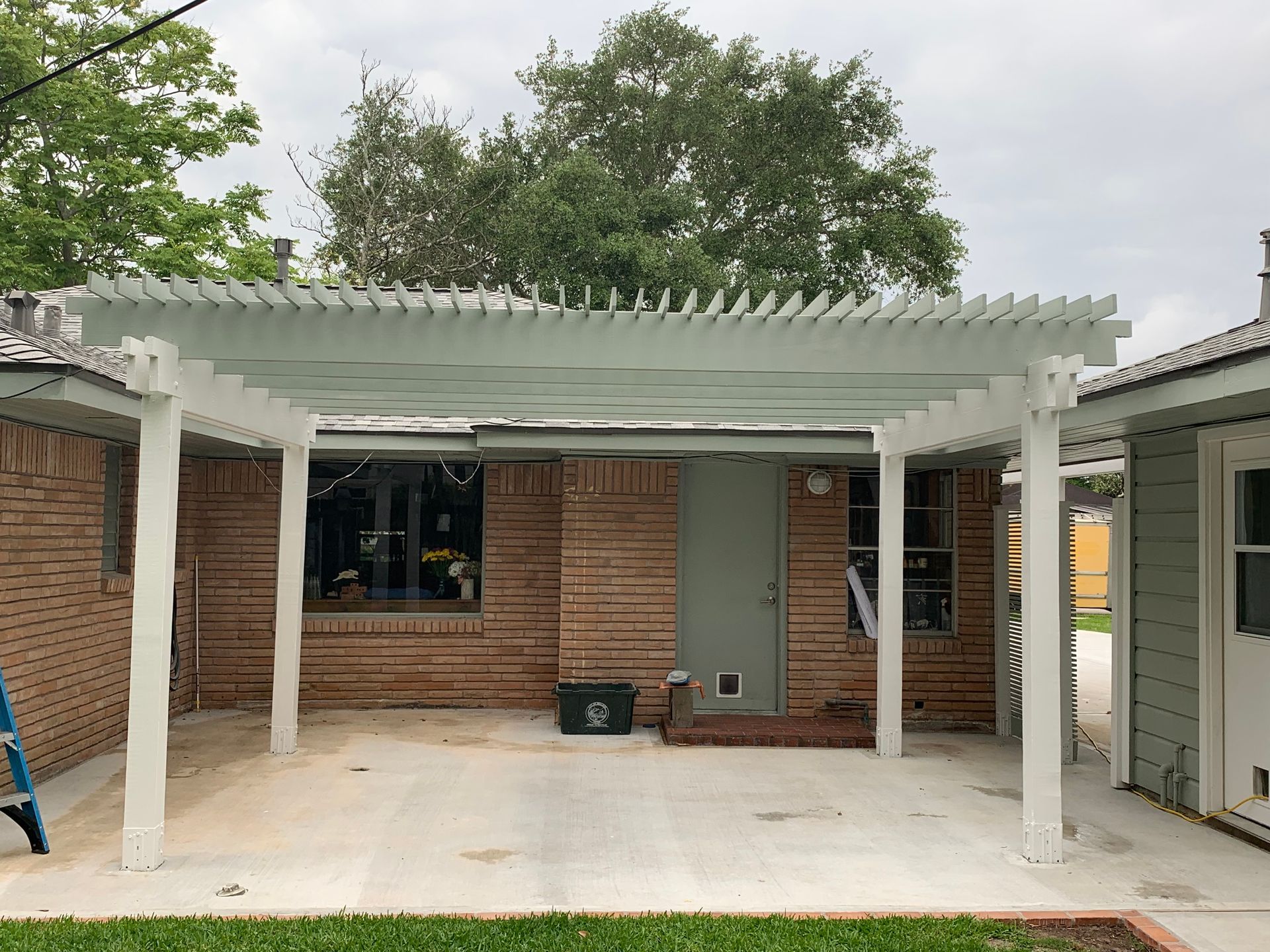 White pergola covering a brick home's patio. 