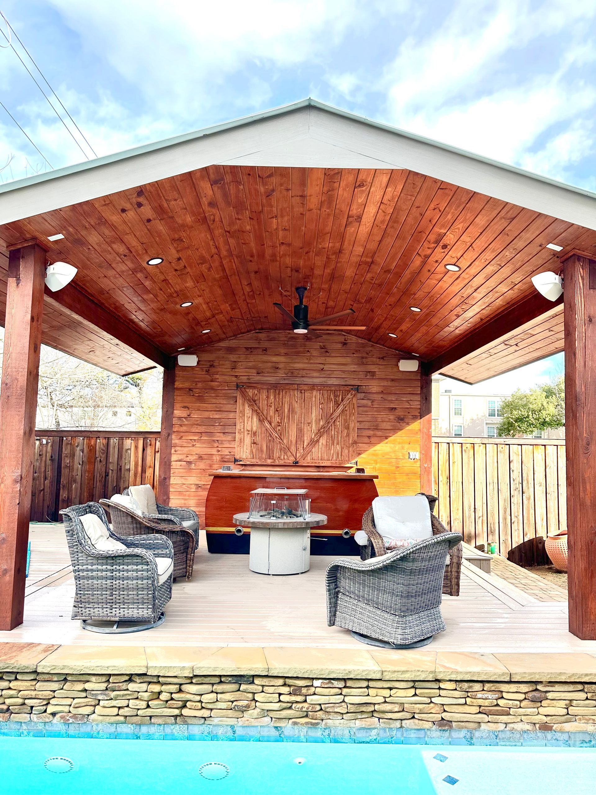 Outdoor patio with wood ceiling, seating area, fire pit, and pool.