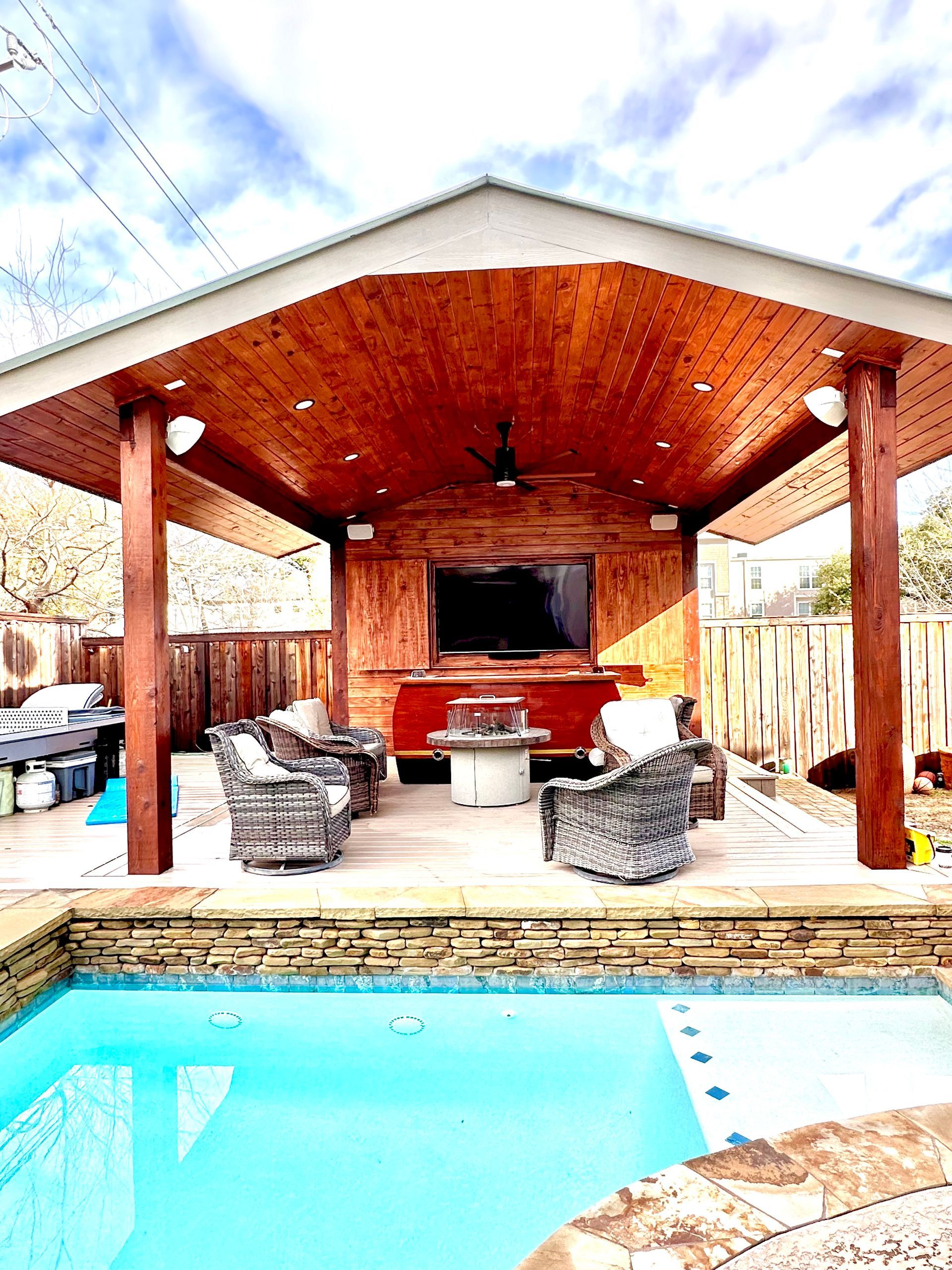 Outdoor covered patio with a pool, seating, and a TV. 