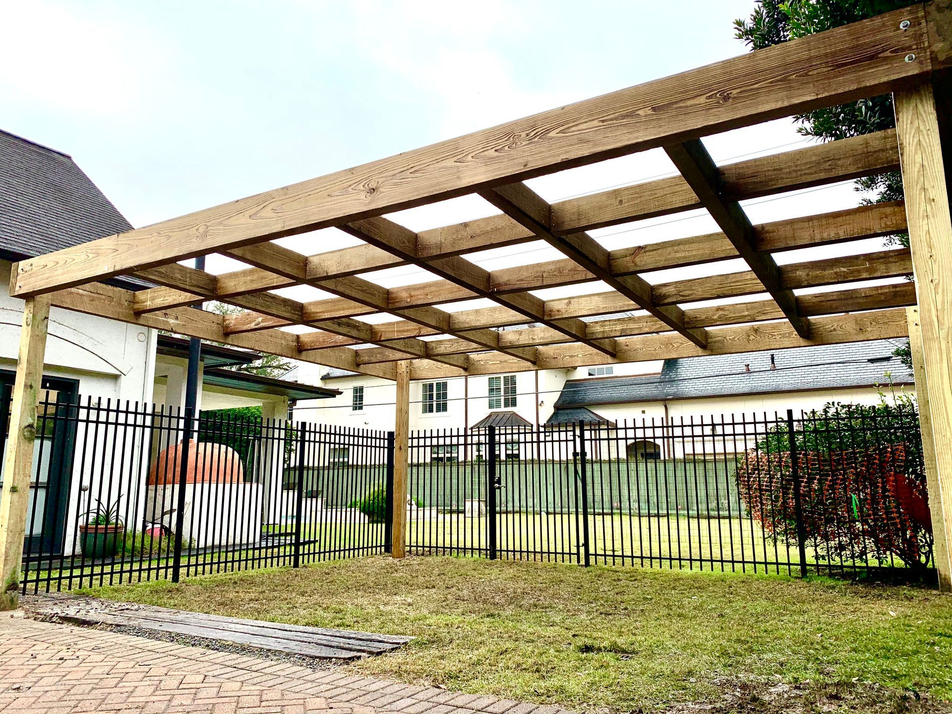 Wooden carport structure over a grassy area, surrounded by a black fence.