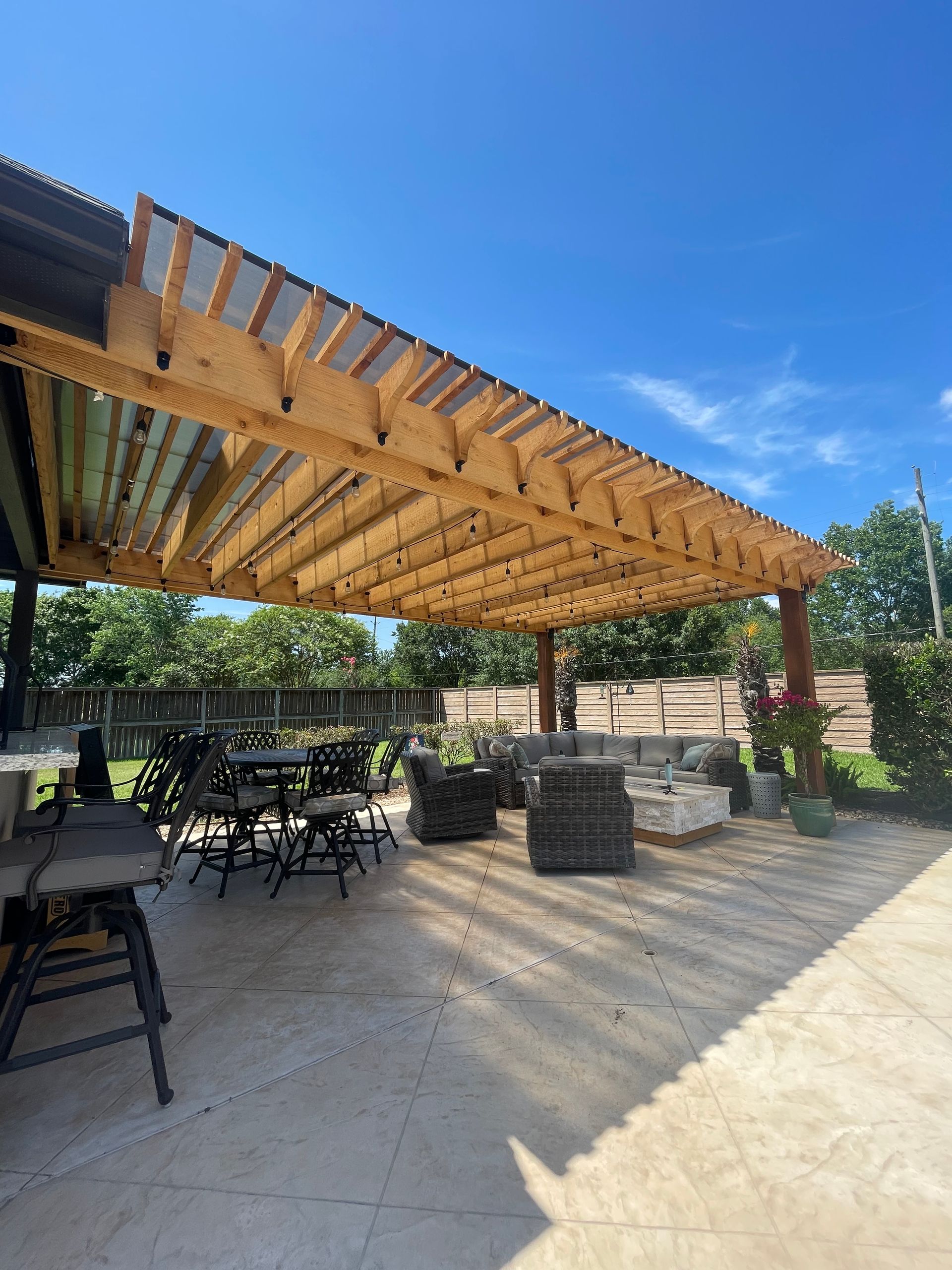 Wooden pergola over patio with seating and plants, under a blue sky.