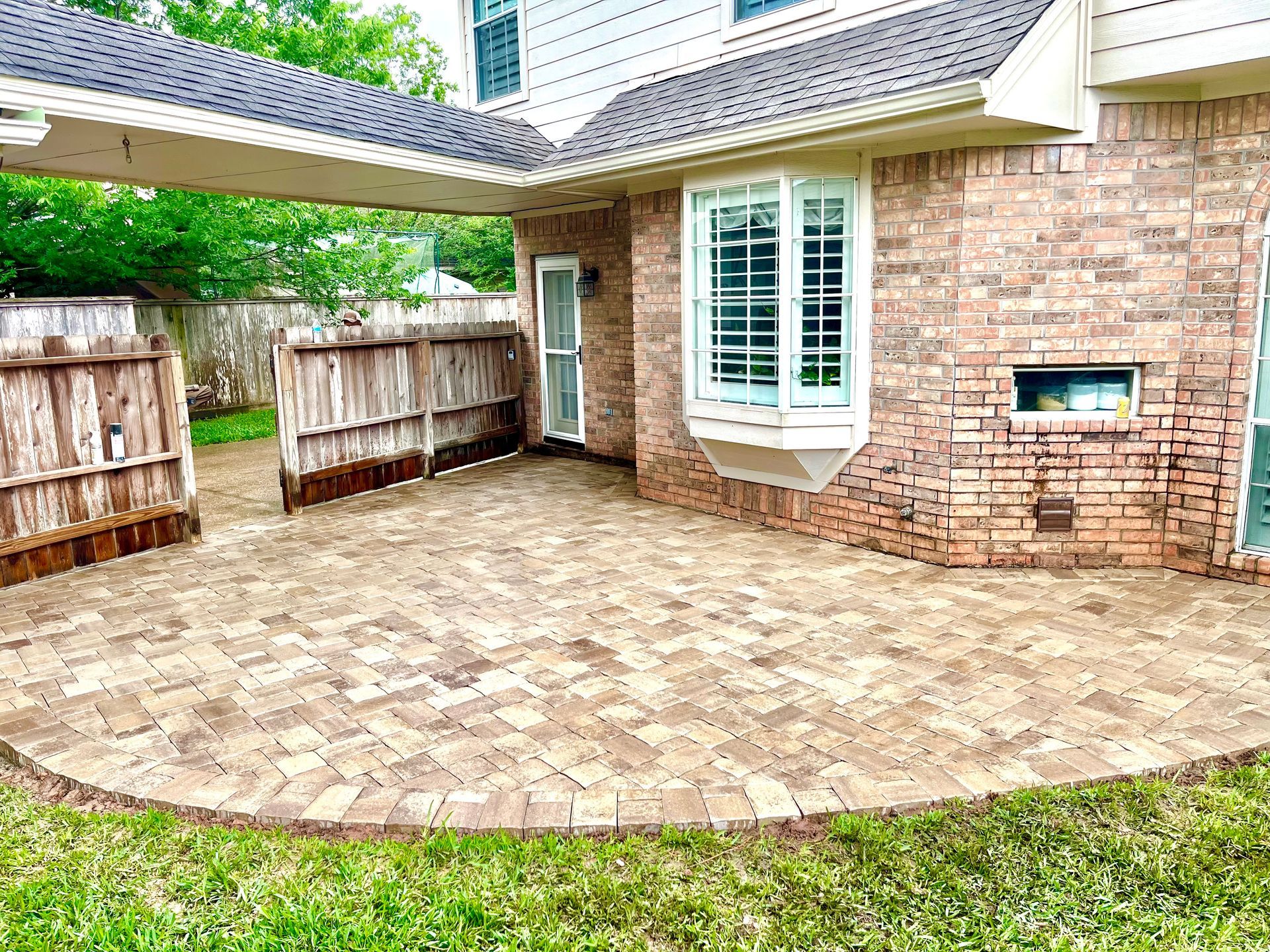Brick patio with curved edge, adjacent to a brick house and wooden fence.