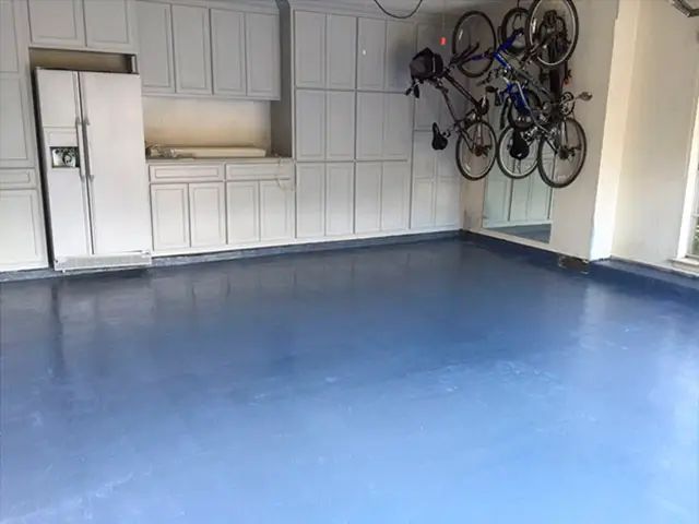 Blue epoxy garage floor with cabinets, refrigerator, and bikes mounted on the wall.