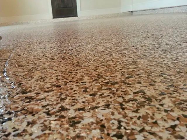 Close-up view of a garage floor with a decorative epoxy coating in shades of brown, beige, and black.