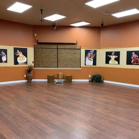 Empty dance studio with hardwood floor, orange walls, and artwork.