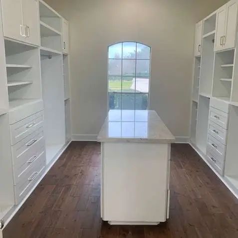 A bright white walk-in closet with shelves, drawers, and an island. 