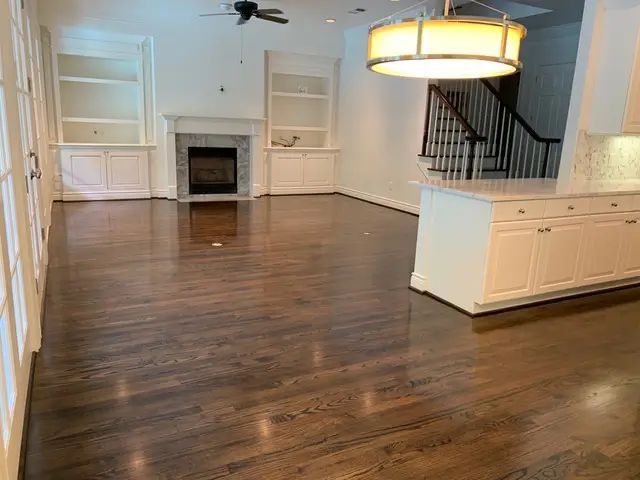 Spacious living area with dark hardwood floors, fireplace, built-in shelving, and a kitchen island.