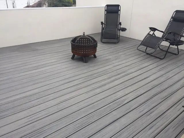 Gray deck with fire pit and two reclining chairs against a white wall.