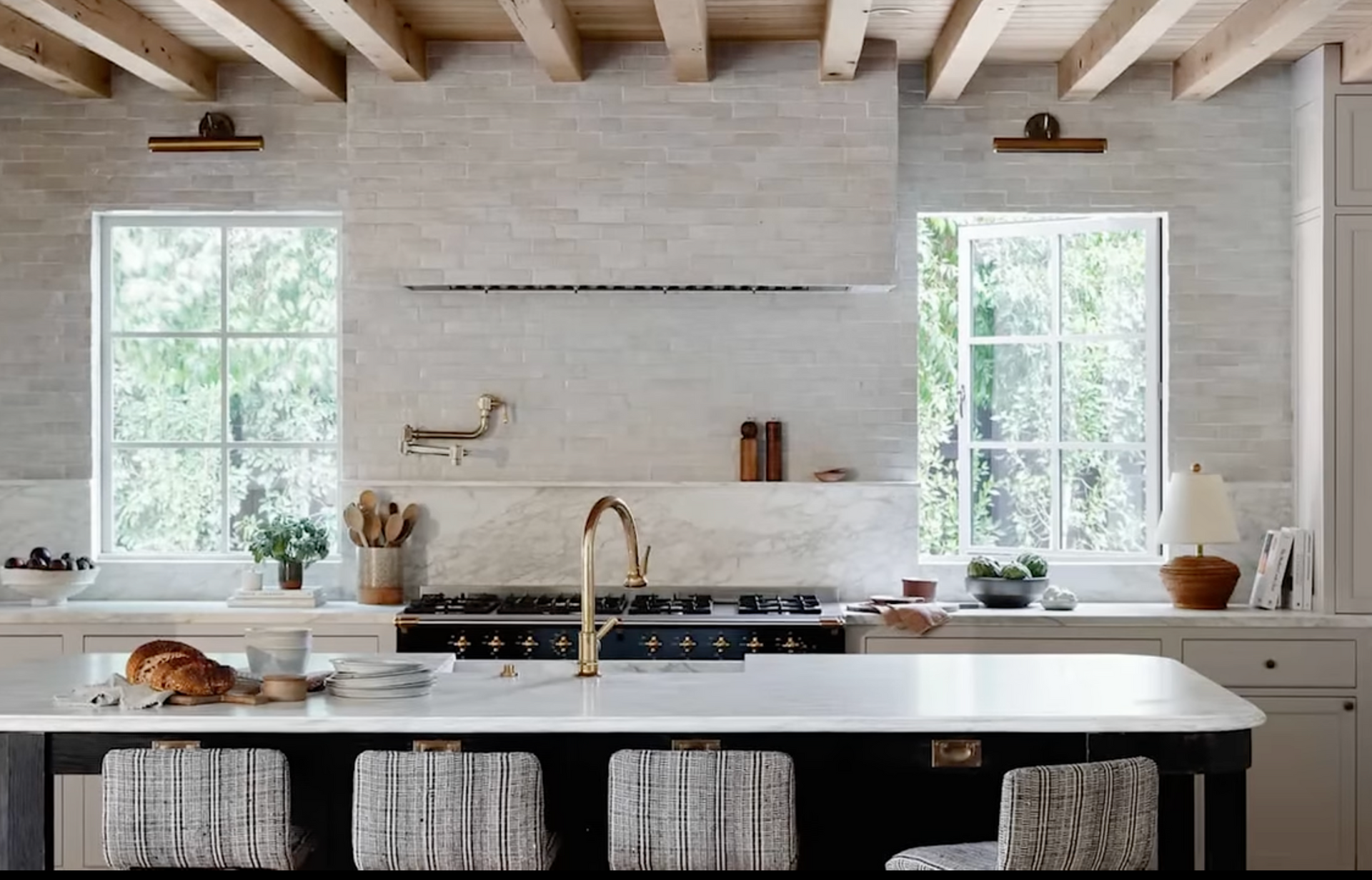 Bright modern kitchen with white brick walls, wood beams, and a large island under two windows