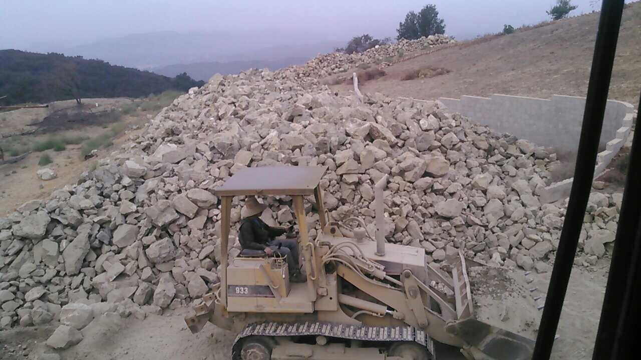 A small yellow bulldozer loads rocks on a construction site, with a person driving.