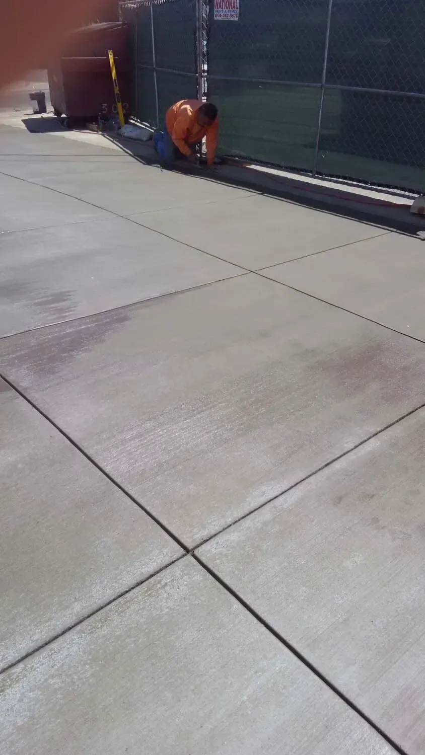 Man cutting lines in fresh concrete sidewalk outside.