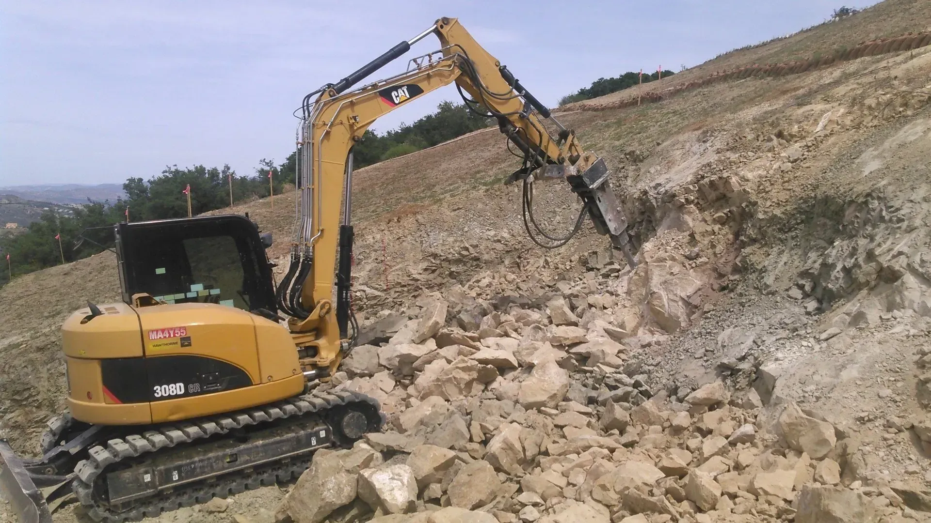 Yellow excavator breaking rock on a hillside.