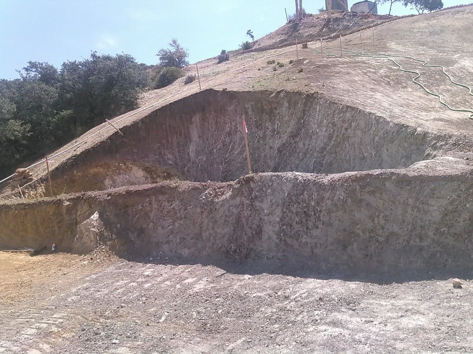 Erosion on a hillside with exposed layers of earth, under a bright sky.