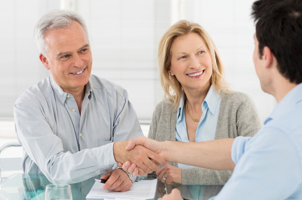 A Man and Woman Are Shaking Hands with A Conveyancer While Sitting at A Table — Pink Conveyancing Services in Port Macquarie, NSW