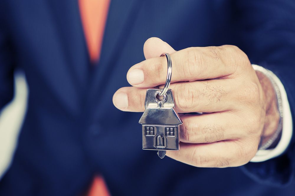 A Man in A Suit and Tie Is Holding a House Keychain — Pink Conveyancing Services in Port Macquarie, NSW