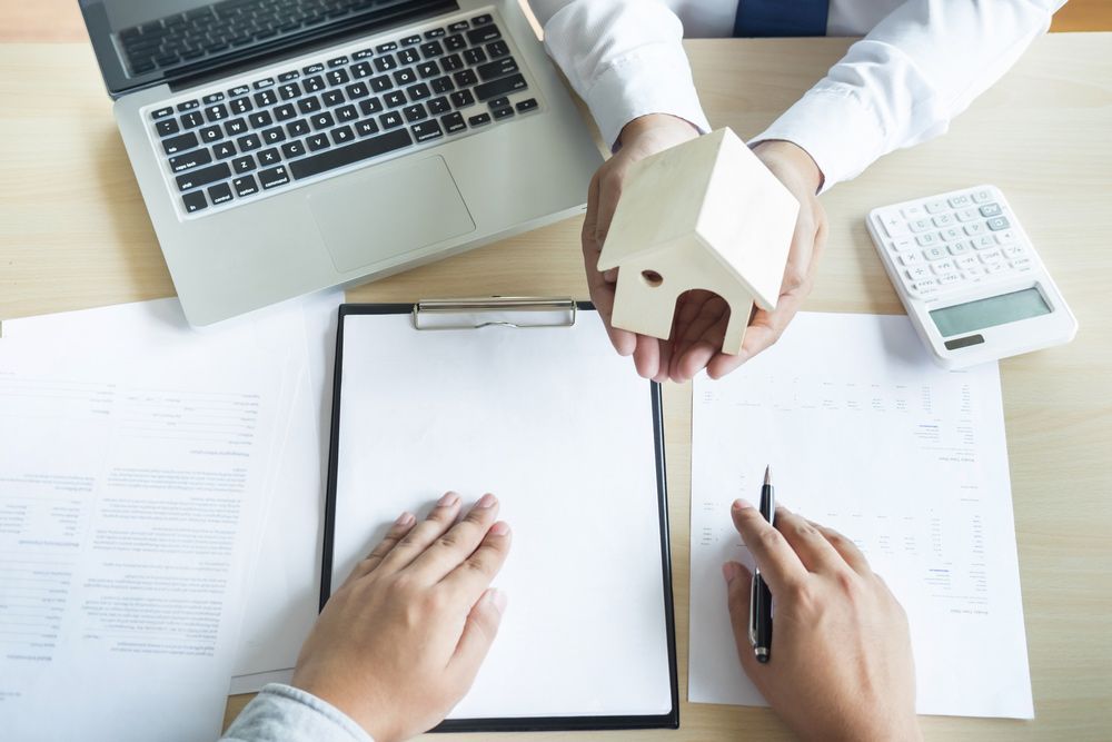A Man Is Holding a Model House in His Hands While a Woman Is Signing a Document — Pink Conveyancing Services in Port Macquarie, NSW
