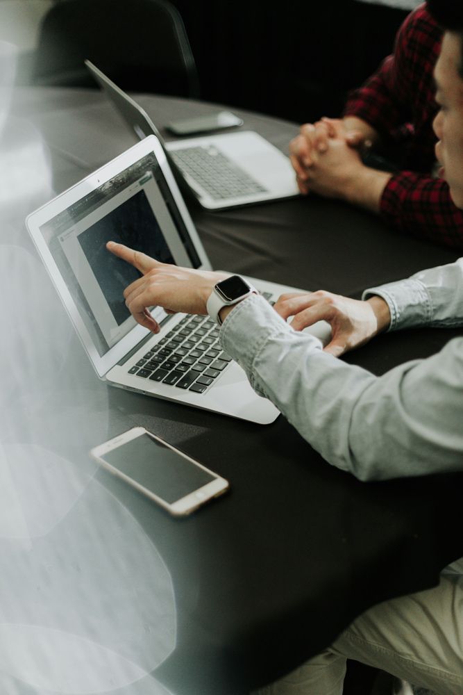 Conveyancer Is Pointing at A Laptop Computer While Sitting at A Table — Pink Conveyancing Services in Port Macquarie, NSW