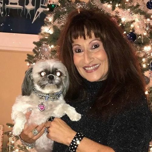 A woman is holding a small dog in front of a christmas tree