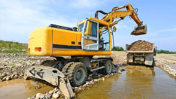 A Yellow Excavator is Loading Dirt Into a Dump Truck — Advanced Industry Training In South Townsville, QLD
