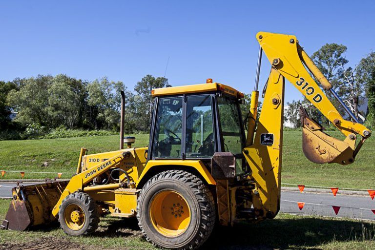 A Yellow Backhoe is Parked in a Grassy Field — Advanced Industry Training In South Townsville, QLD