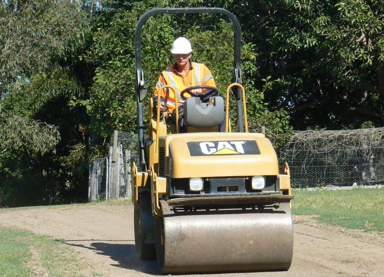 A Man is Driving a Cat Roller on a Dirt Road — Advanced Industry Training In South Townsville, QLD