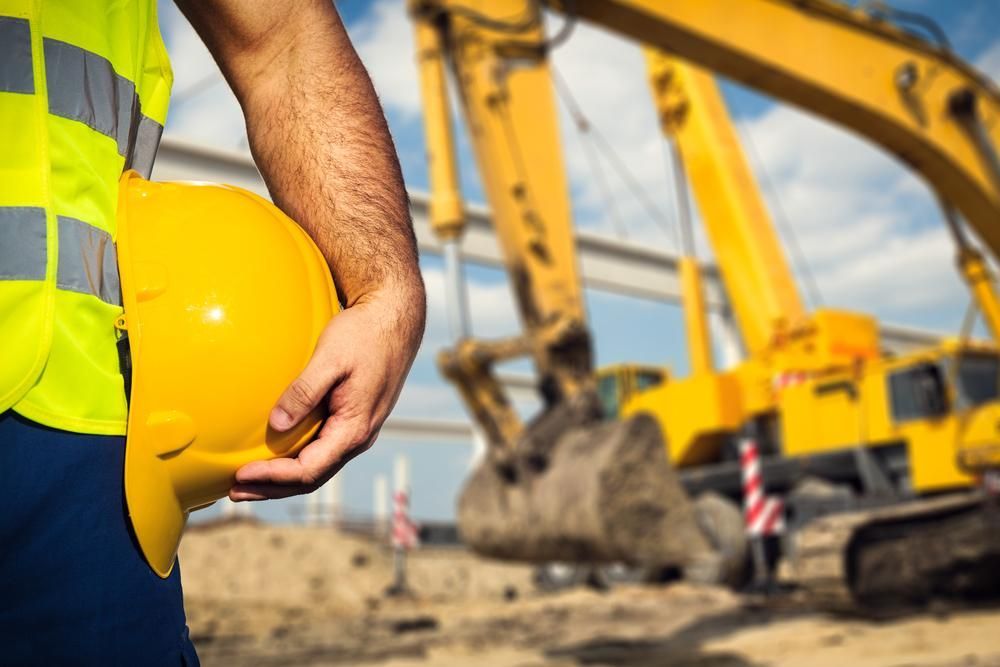 A Worker is Holding a Yellow Hard Hat at a Construction Site — Advanced Industry Training In South Townsville, QLD