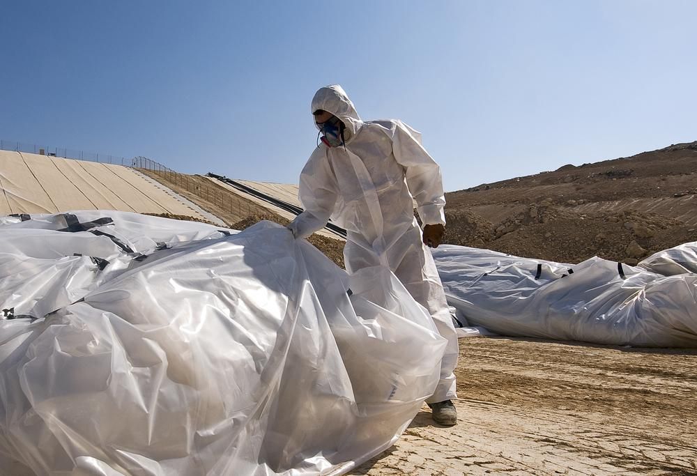 A Man in a Protective Suit is Holding a Plastic Bag — Advanced Industry Training In South Townsville, QLD