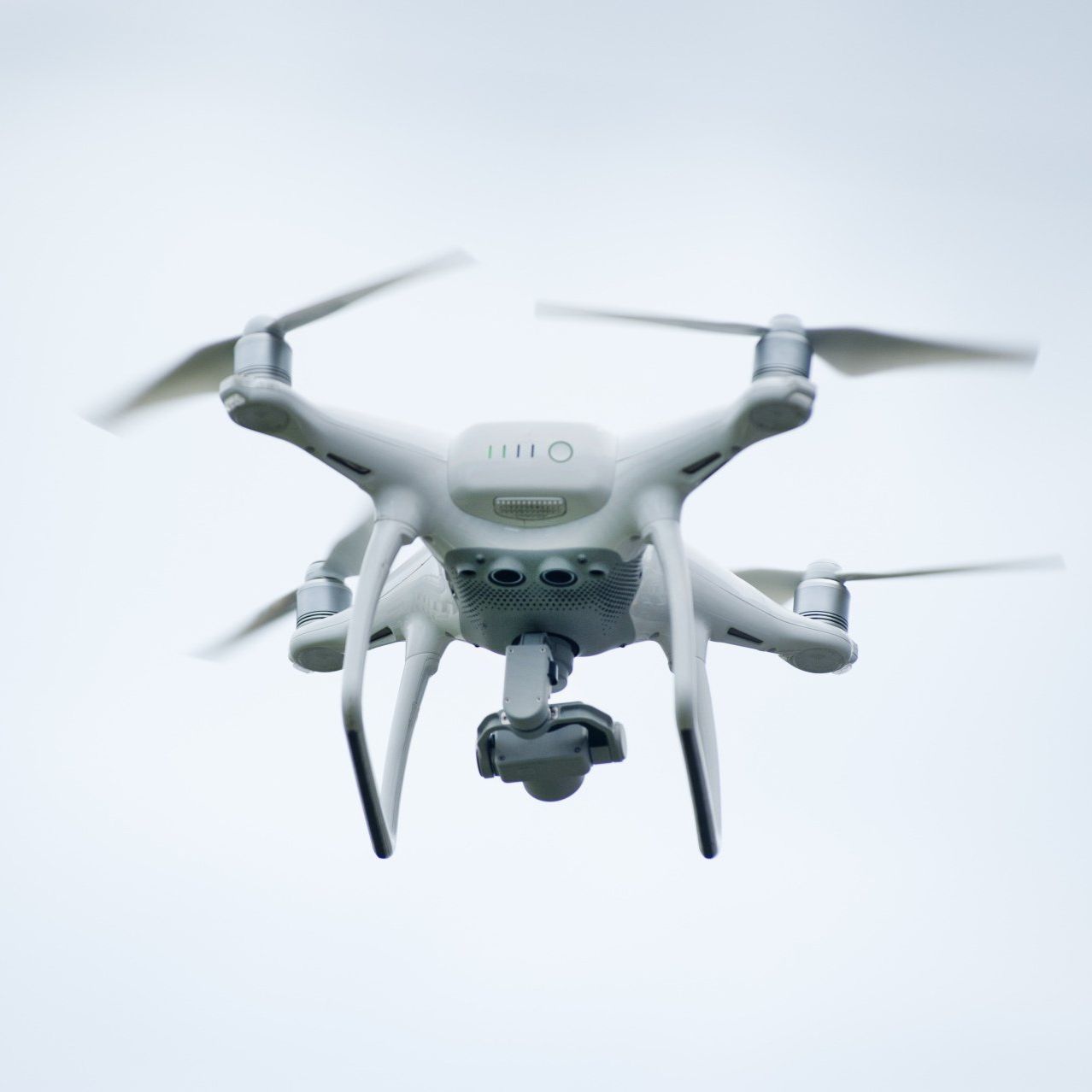 A white drone is flying through a cloudy sky