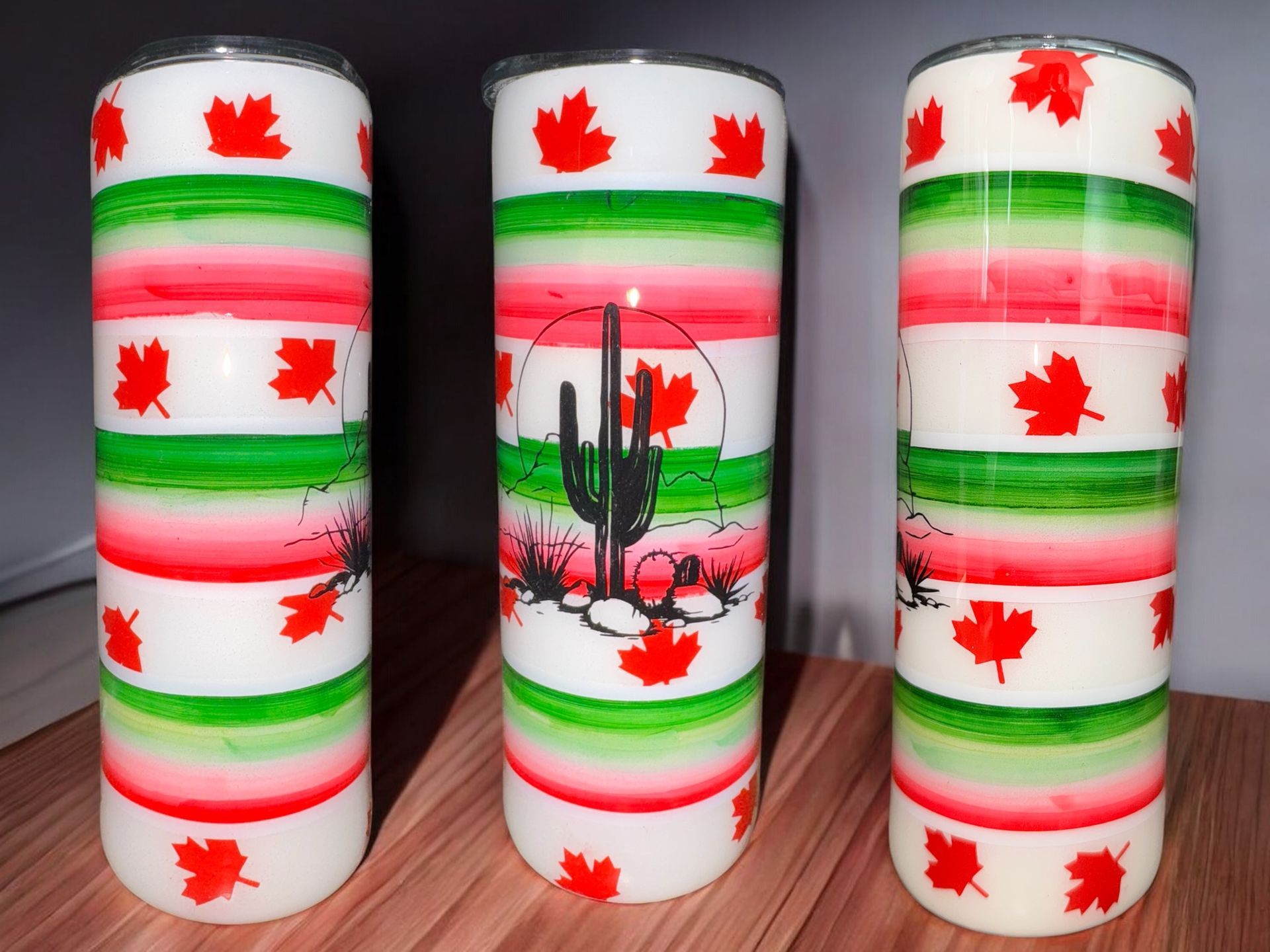 Tumbler with desert cactus design, red and green stripes, maple leaves, on a wooden surface at sunset.