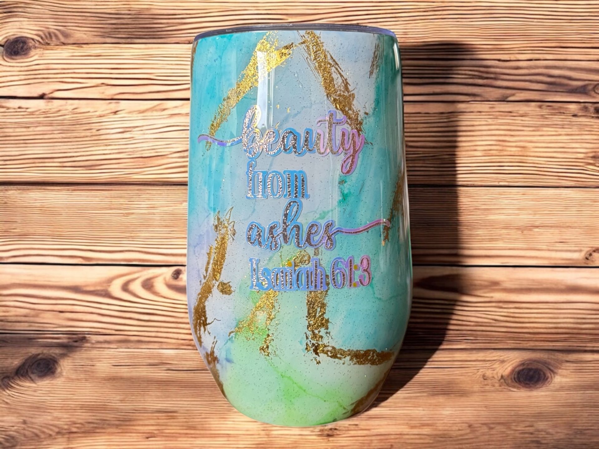 Three stemless wine tumblers with watercolor-like swirls of blue, green, and gold, with gold accents. The center tumbler has the inscription 
