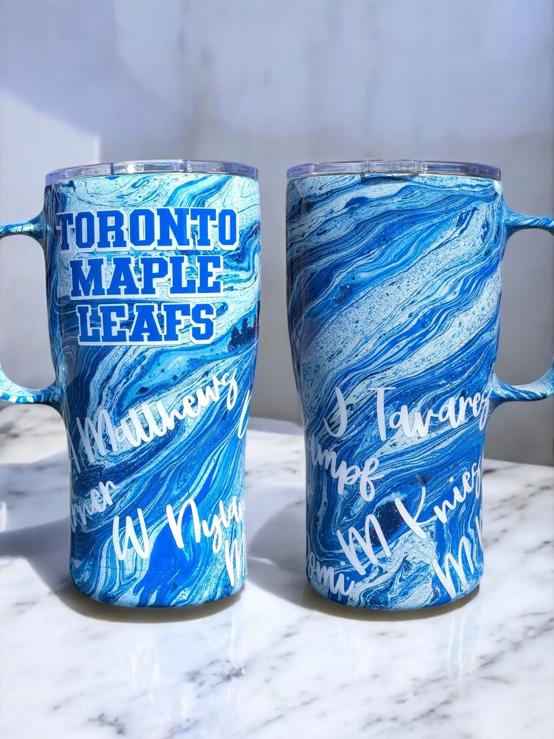 Toronto Maple Leafs tumbler with blue and white swirl design, handle, on wooden table with coffee beans.