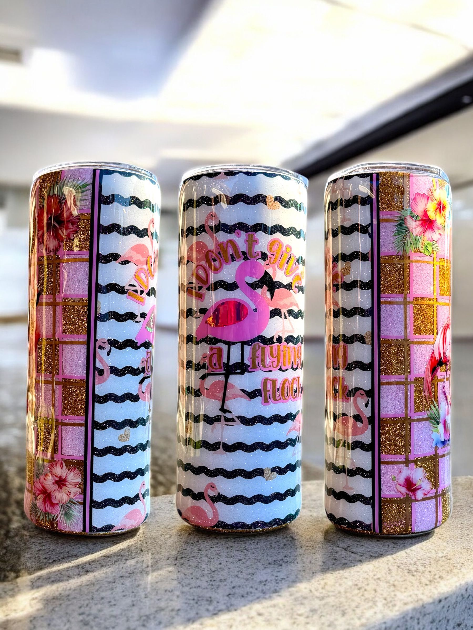Three glittery flamingo-themed tumblers with floral and striped designs.