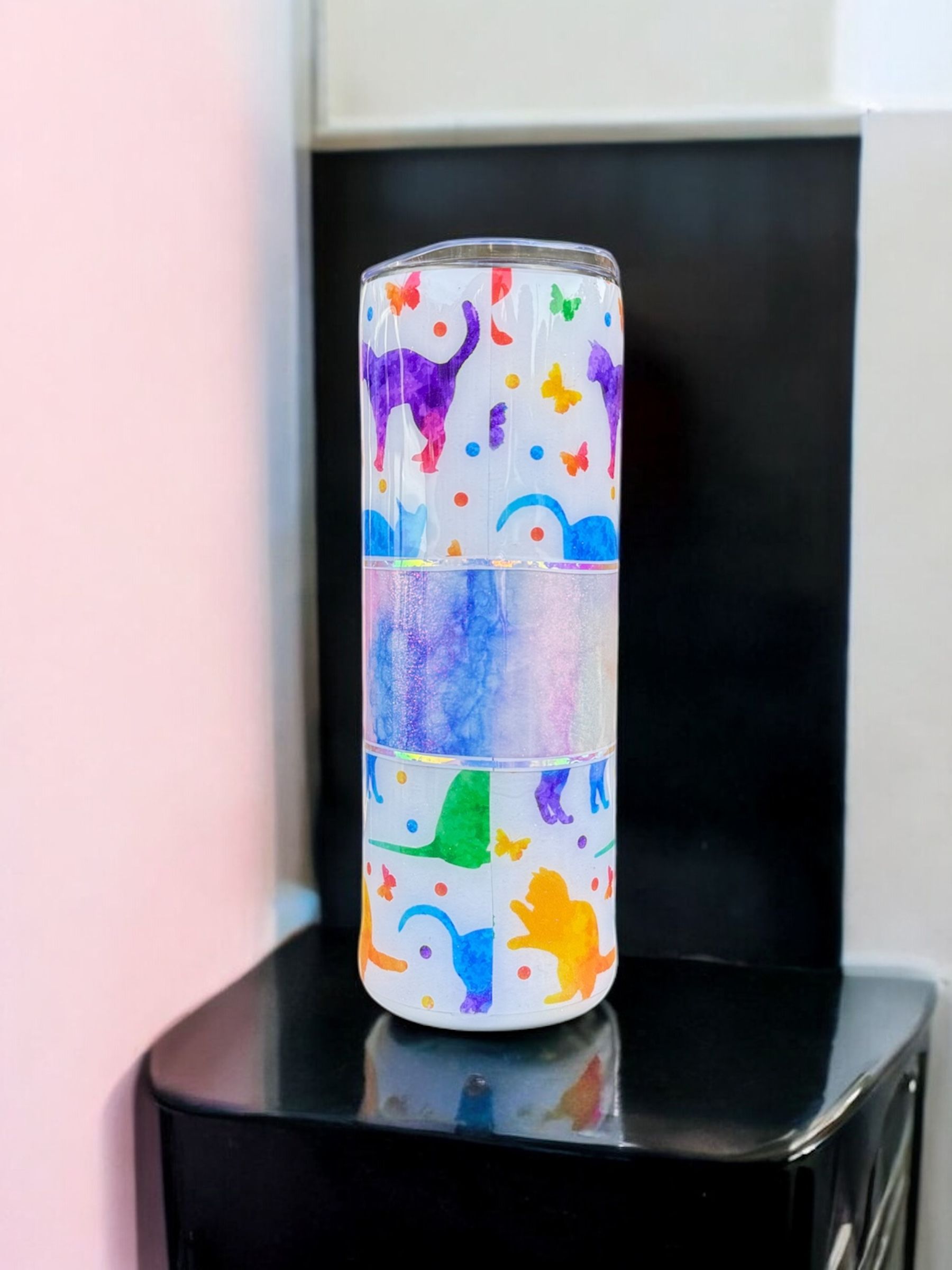 A custom-decorated tumbler with dinosaur and butterfly designs, set on a black surface.